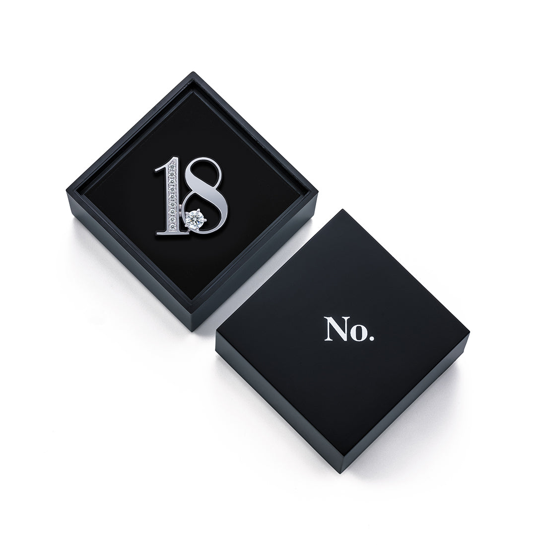 黒い正方形のギフトボックスに収められた、No.のNo.18ダイヤモンドラペルピン。ジュエリーの輝きを引き立てる上質なパッケージデザイン。